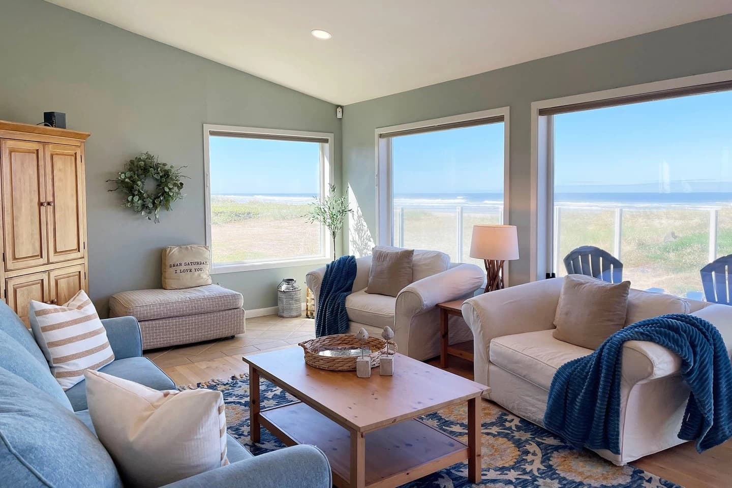 Waldport living room with cream chairs, a blue sofa, and windows to dunes and ocean