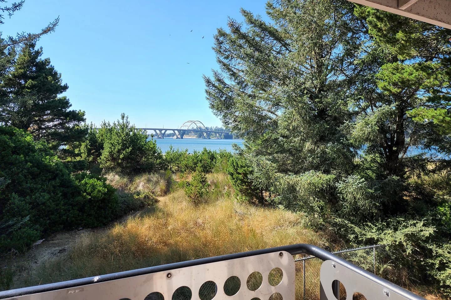 Balcony with circular-cutout railing overlooks grassy dunes and a bay in Waldport