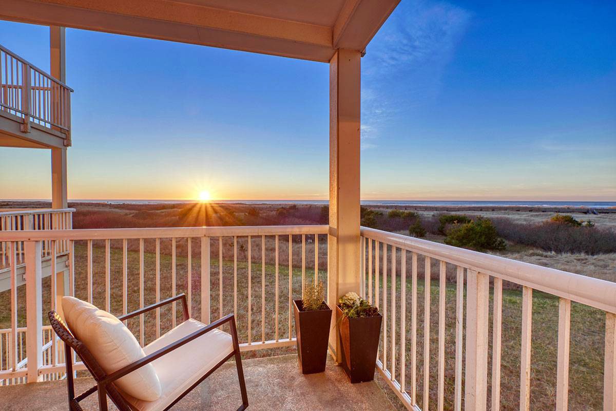 Cushioned chair overlooking ocean view sunset from corner balcony of condo.