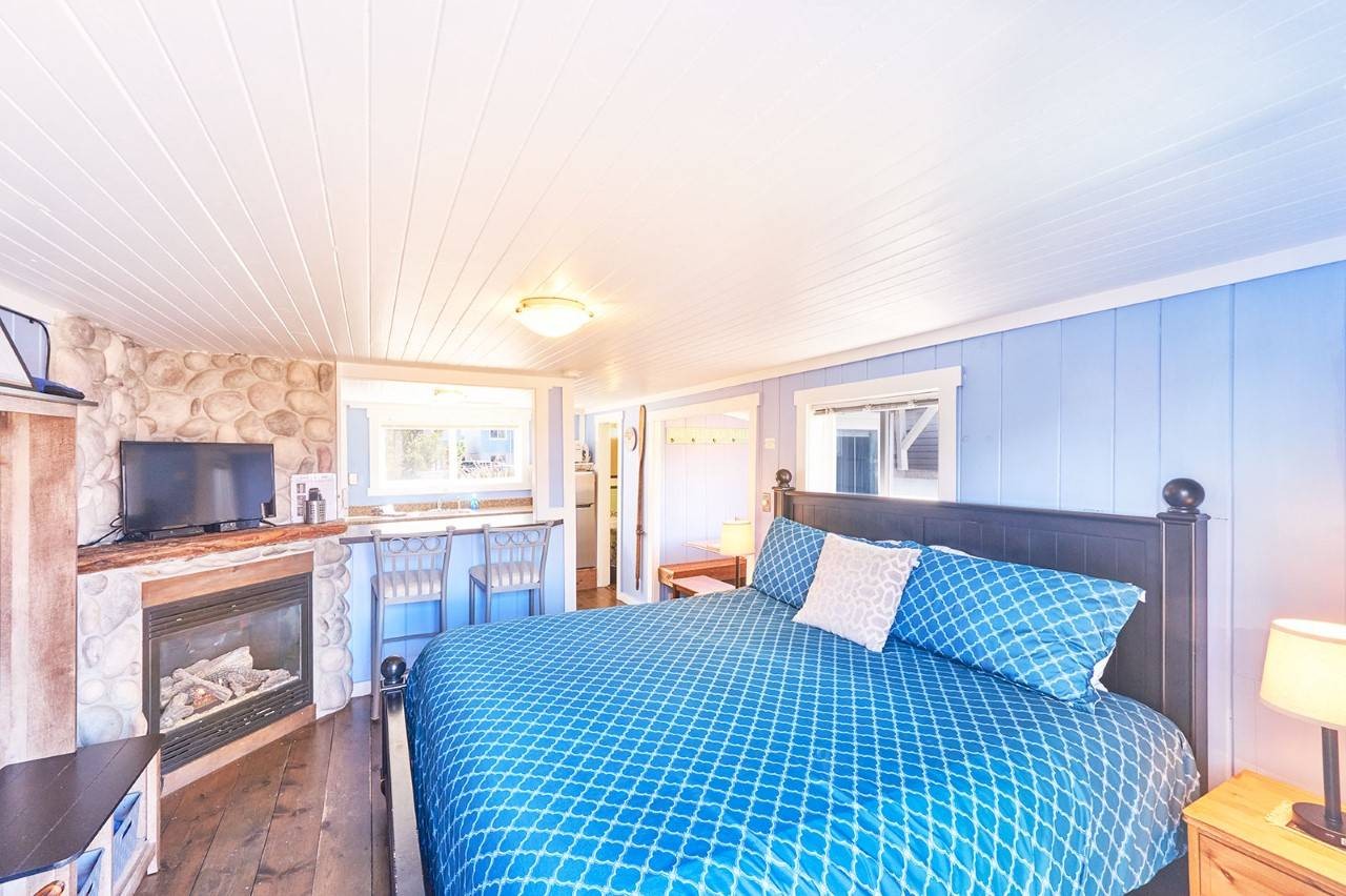 Two chairs and table on a fenced deck surrounded by a green grassy yard and other houses.