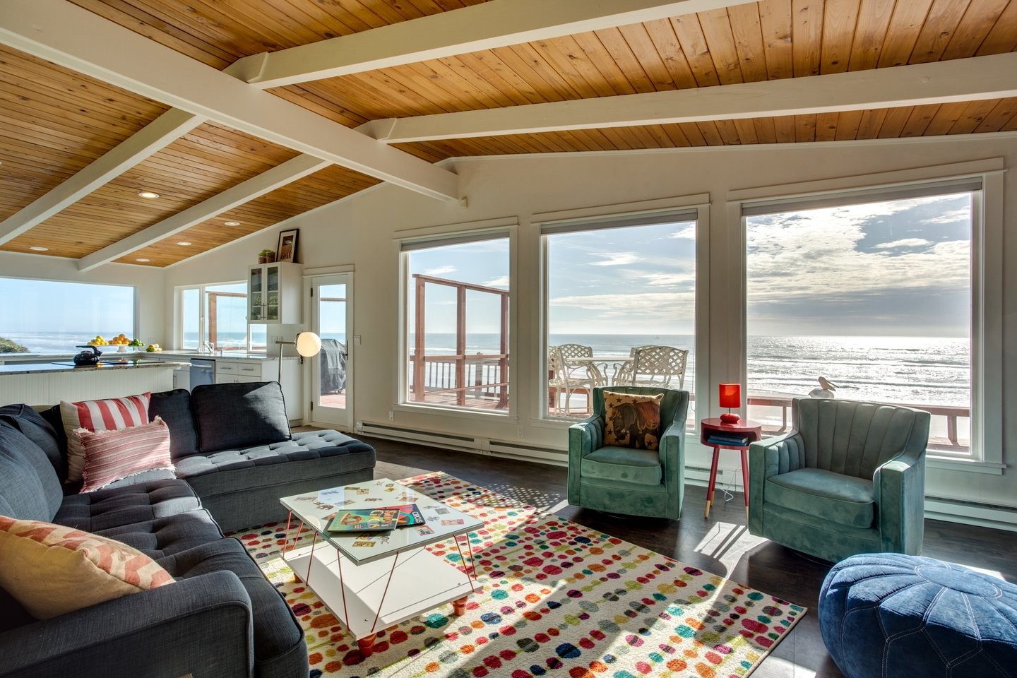 A large open living room surrounded by windows, a large deck, and oceanfront views.