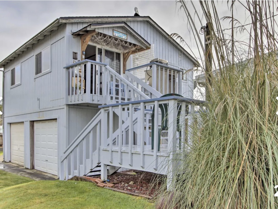 Tall grass plant in front of a 2 level gray double car garage with 2 flights of stairs and sliding glass doors.