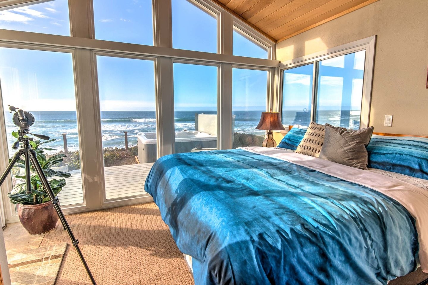 A beautiful turquoise and tan bedroom with surrounded by windows with oceanfront views and a hot tub.,