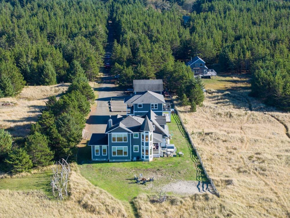 Aerial view of 3 beach houses sitting in a green grassy mowed area, private beach path through grassy dunes, and fir trees in the back.