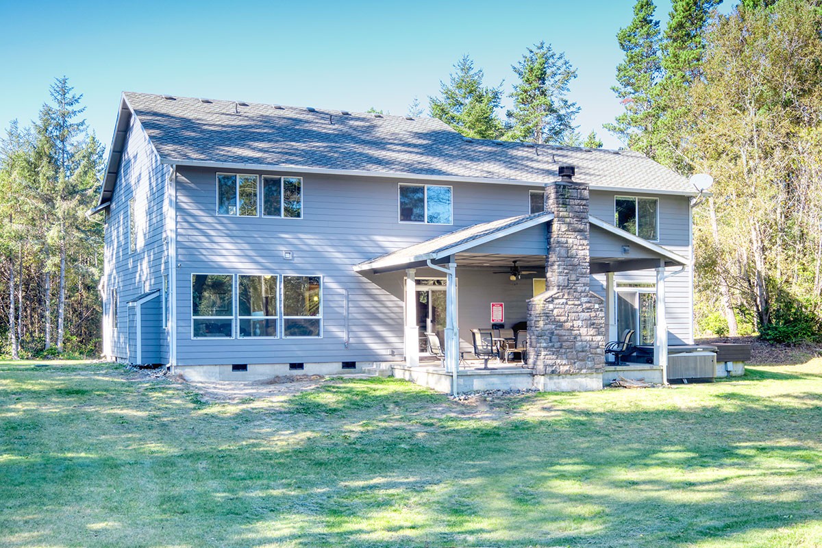 Lake view covered patio with fireplace, tables, chairs, and gas grill.