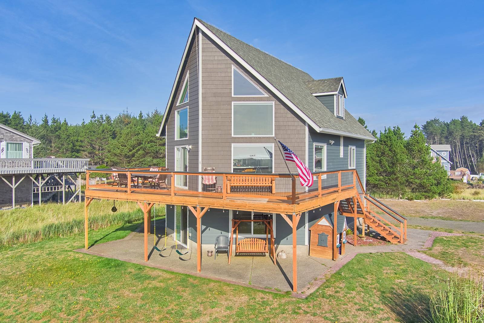 Three-level beach house with prow front windows, wrap around deck, and large grassy yard.