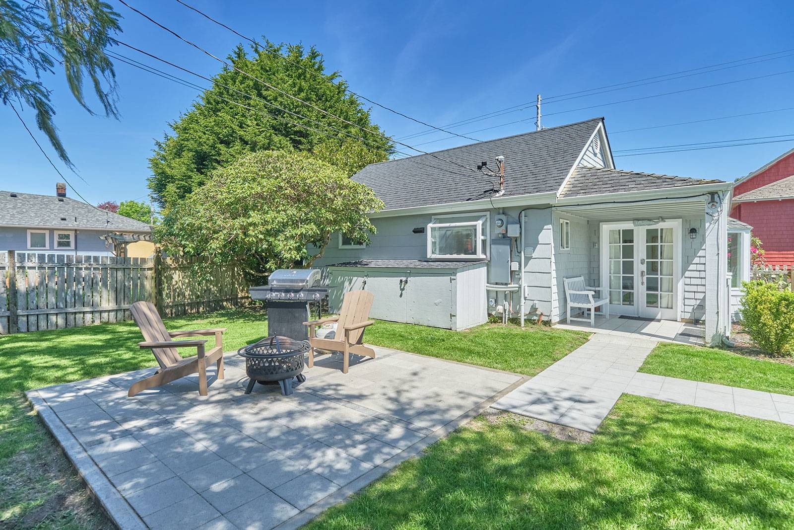Small gray cedar shake beach cottage, big window, covered porch, and fenced yard.